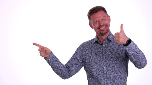 Smiling recommends empty area on white background and advertises dots in empty space. Man using thumb up and best choice sign mockup for promotional advertisement