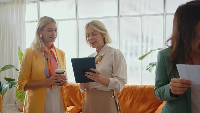 Cinematic footage of a multiethnic group of women managing new projects in a start up business. Female colleagues working as a team in the office wearing elegant colored diverse outfits