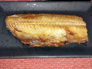 焼き魚ホッケが黒い皿の上にのっている