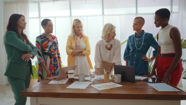 Cinematic footage of a multiethnic group of women managing new projects in a start up business. Female colleagues working as a team in the office wearing elegant colored diverse outfits