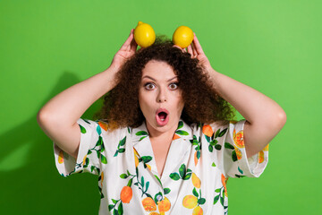 Portrait of impressed lovely girl hold fresh lemons head make ears open mouth isolated on green...