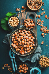 Nuts background. Hazelnuts in a bowl, nut kernels and Nutcracker, tongs for nuts on a dark stone table. Vertical photo.