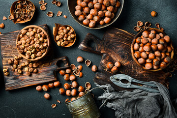 hazelnuts in shells scattered from a vintage burlap sack onto dark background. Some are shelled and...