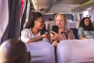 Jovem ensinando mulher idosa a usar o aplicativo de transporte urbano em seu smartphone, durante viagem de onibus. - obrazy, fototapety, plakaty