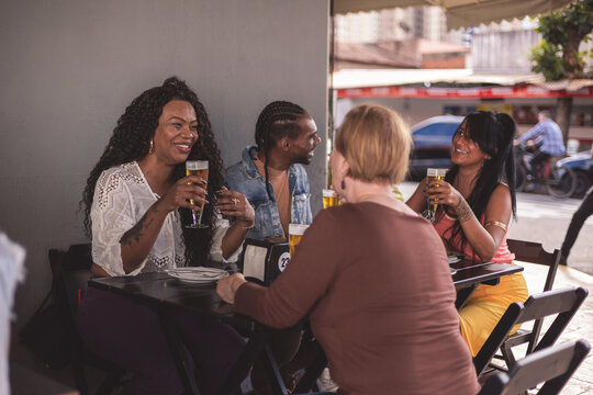 Pessoas felizes de diferentes idades desfrutando de uma bebida em bar ao ar livre.