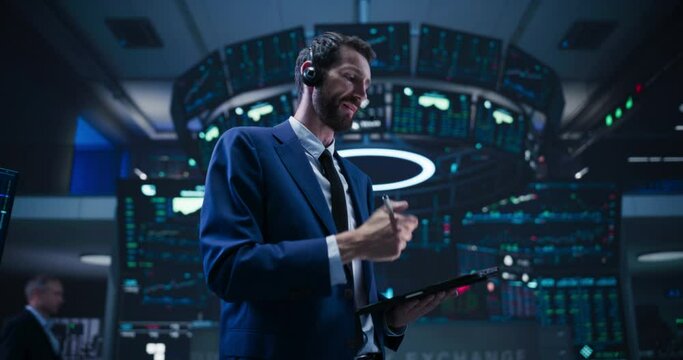 Low Angle Portrait of an Energetic Stock Exchange Manager Working in Modern Office. Proactive Trader Communicating Orders with a Headset and Microphone, Talking on a Call with Auction Operators