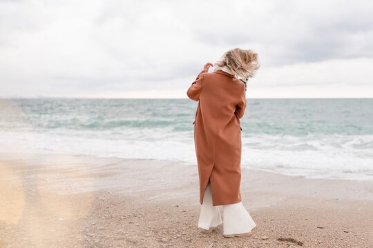 Blond woman Christmas tree sea. Christmas portrait of a happy woman walking along the beach and holding a Christmas tree in her hands. She is wearing a brown coat and a white suit.