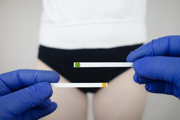 Bacterial Vaginosis. Vaginal pH. Girl shows sticks for measuring acid-base balance of genital organs. Self-diagnosis. Normal acidity level shown in colors and must be compared with the standard