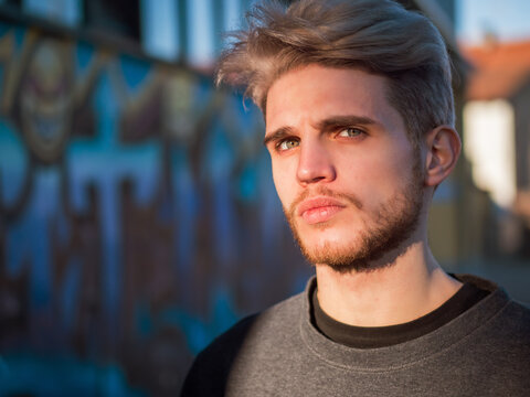 A man with blonde hair standing in front of a wall. Photo of a man with blonde hair standing in front of a wall, looking at camera