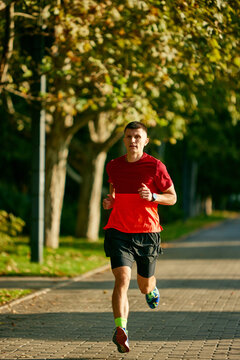 Dynamic image of young muscular man, athlete in motion running in early morning in park, training outdoors. Concept of sport, active and healthy lifestyle, competition, dynamics, marathon