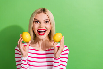 Fototapeta na wymiar Photo of laughing positive mood youngster girl red lipstick optimistic wear striped top hold two lemons isolated on green color background