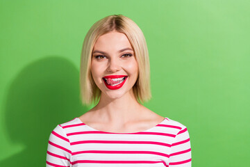 Photo of good mood girlish woman with bob hairstyle dressed striped stylish shirt licking teeth isolated on green color background