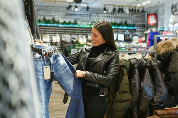 Fototapeta premium Adult smiling girl buying pants in clothing store