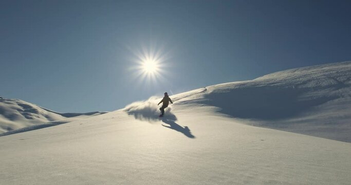 Man on snowboard slides down mountain. Professional snowboarder slides down and braking sharply covers shot with avalanche of white snow shining in sun. Extreme sport energizes and keeps in good mood