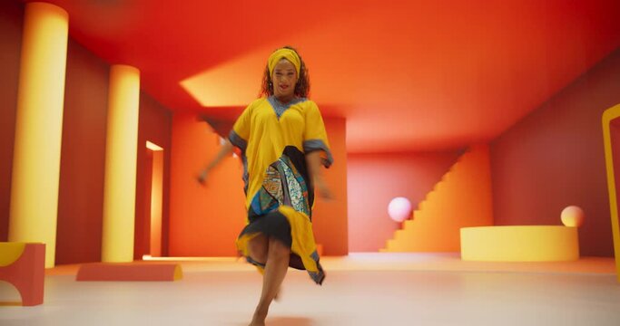 Beautiful Black Woman in African Outfit Dancing Energetically in Geometric Abstract Orange Environment. Creative Female Performing Modern Dance Choreography in a Studio While Looking at the Camera
