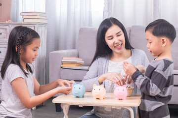 Asian family teaching children saving in piggybank, practicing finance planning for future, mother put coins in piggy bank and encourage children to be disciplined to save money left from school