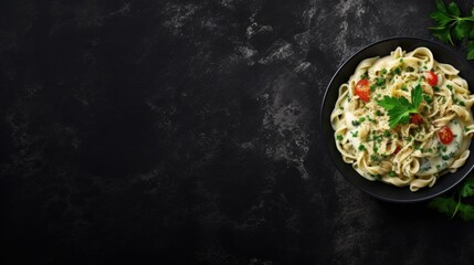 Pasta with green vegetables and creamy sauce in black bowl on grey stone background. Top view. Copy space.
