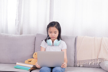 Asian preteen schoolgirl doing homework on digital modern technology laptop, kid elementary girl using gadget study with distance homeschool online learning stay at home, education for student work