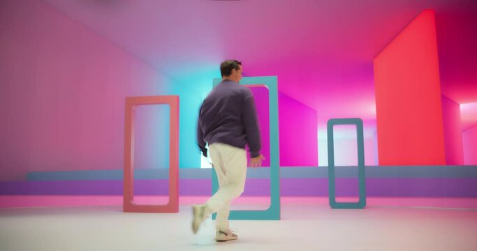 Young And Athletic B-Boy Breakdancing To Break Beats in a Colorful Abstract Neon Lit Studio. Energetic Fashionable Male Dancer Performing Talentedly Performing While Looking at the Camera