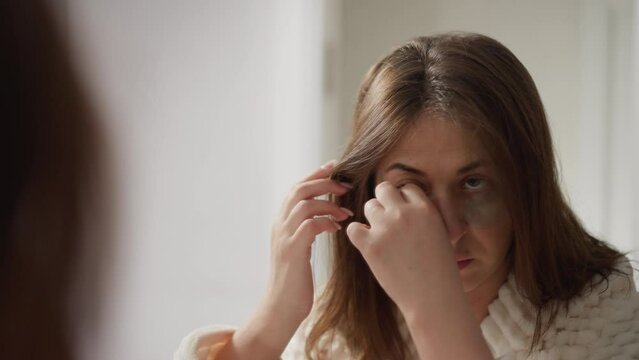 Pretty lady removes eye patches admiring result in mirror. Young brunette with short hair examines quality of skin after using cosmetic product