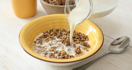 Milk is poured into a plate with granola or muesli. Healthy food. Preparing breakfast. Close-up.
