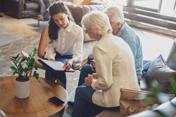 A hotel or travel agency representative is talking with a senior tourist couple offering various...