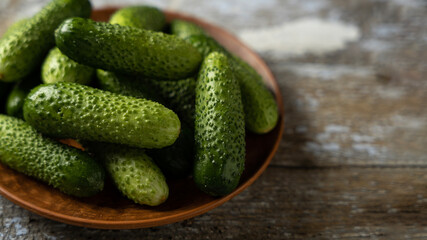 Green cucumbers on a plate, old wooden background, banner, space for text