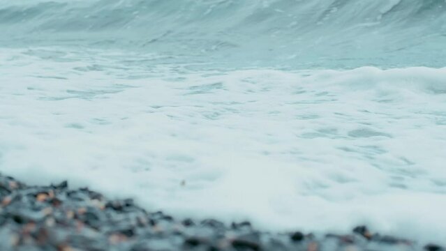 Sea cost. Sea waves. Sand coast. Rush of water. Blue waves. Summer location. Holiday trip. Nature. Small stones on the shore. Black rocs
