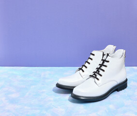 Two convenient white leather boots with black soles and shoelaces are on the table. Boots for winter or cold autumn. Closet and fashion idea. Copy space for text.