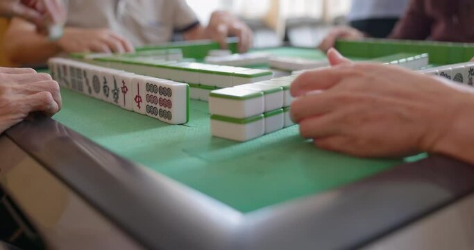 Selective focus with closeup of mahjong tiles and the player's hand tapping on gambling table.