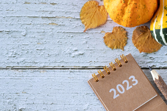 Autumn leaves and pumpkin with spiral calendar 2023 year on rustic wooden background. Thanksgiving day concept. Top view. Copy space. - Powered by Adobe