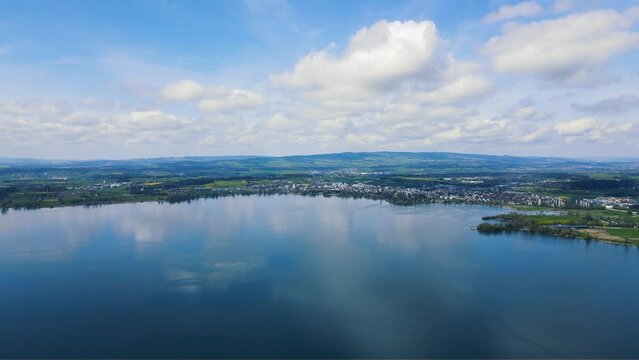 panoramic aerial view of idyllic Swiss Lake Zugersee with glassy crystalline water surface in the Alps of Switzerland featuring yellow fields, village of Cham, and swiss alpine sceneries 