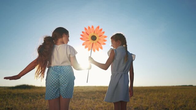 child girls standing lifestyle with windmill a toy in the park. happy family kid dream concept. daughters girls playing with toy windmill in nature. childhood freedom wind lifestyle concept outdoors