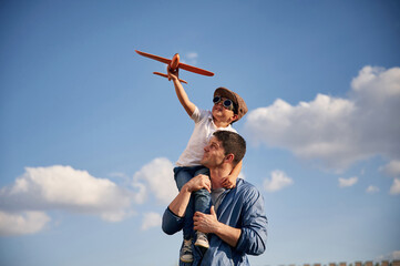 With aviator glasses, playing with toy plane. Father and little son are having fun outdoors - obrazy, fototapety, plakaty