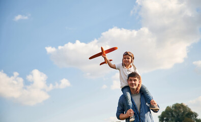 With aviator glasses, playing with toy plane. Father and little son are having fun outdoors