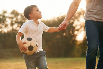 Holding hands and soccer ball. Father and little son are playing and having fun outdoors - obrazy, fototapety, plakaty