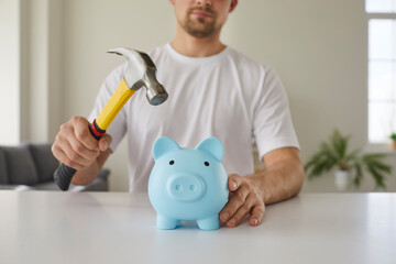 Man wants to break his piggy bank and take the money he has saved up. Young man sitting at table...