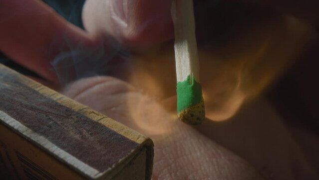 Hands lights a match with a green sulfur head, slow motion. Strikes a match on the side of the box. Smoke and fire appear. The flame ignites. The match lights up, burns and goes out. Super macro shot