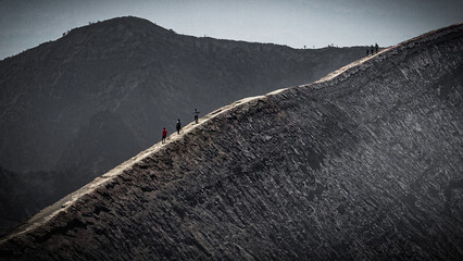 Tourists on the Bromo volcano walking along the rim of the crater against the backdrop of the mountain in gray colour palette in Taman Nacional Park on Java, Indonesia © Kosma Sobol