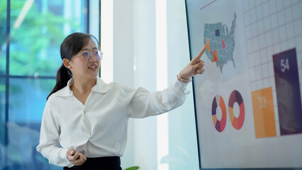 young asian business woman standing in front of television screen giving presentation and Explaining Graphs in office . speaker with whiteboard presenting  idea to colleagues in meeting