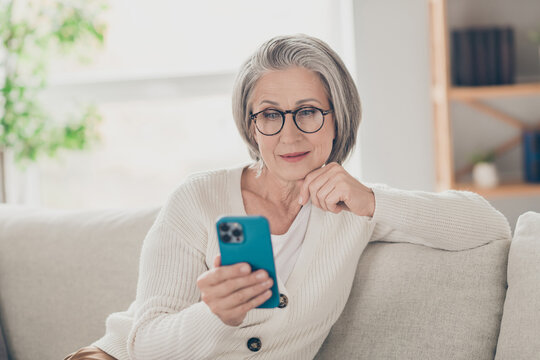Photo of thoughtful clever senior lady dressed white cardigan eyewear reading apple samsung iphone modern device indoors house room