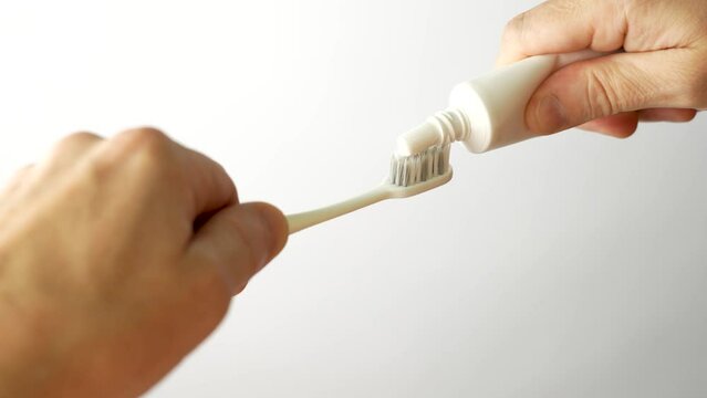 Hands applying toothpaste to a toothbrush, close-up