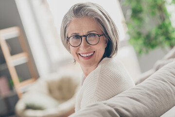 Fototapeta premium Photo of adorable pretty senior lady dressed white cardigan eyewear smiling indoors house room