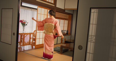 Portrait of a Beautiful Japanese Model Posing in Pink Kimono Outfit. Young Attractive Female Standing in a Room at Home with Traditional Interior. Woman Looking at Camera and Slowly Turning Round