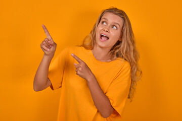 Fototapeta na wymiar Young shocked expressive Caucasian woman teen points to side and opens mouth feeling fear and trepidation from unexpected advertising or large discounts stands posing on yellow background.