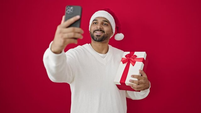 African american man taking a selfie picture holding christmas gift over isolated red background