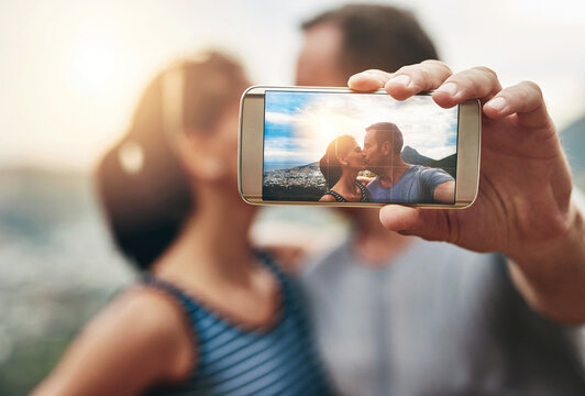 Phone, selfie and couple kiss in nature outdoor on summer vacation together. Smartphone screen, romance and picture of man and woman in countryside for connection, memory of love and relationship