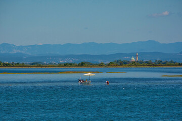 Fishing for cockles from a speed boat in the Grado section of the Marano and Grado Lagoon in Friuli-Venezia Giulia, north east Italy. The Santuario di Barbana Church is seen in the background. August