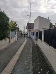 Rue ou ruelle urbaine fort bien éclairé par le Soleil, réflexion lumière, avec un magnifique ciel bleu nuageux, beau jour, début de journée matinale, vide, tranquille, sympathiques maisons , facteur