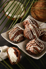 Chocolate profiteroles, eclairs, with coconut cream on a dark background, vertical format